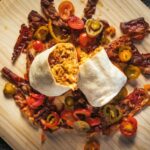 a wooden cutting board topped with a burrito filled with meat and veggies