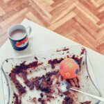 a dog sitting next to a plate of food and a cup of coffee