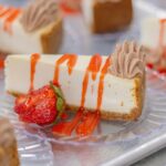 Cheesecake slices are garnished with strawberries and sauce.
