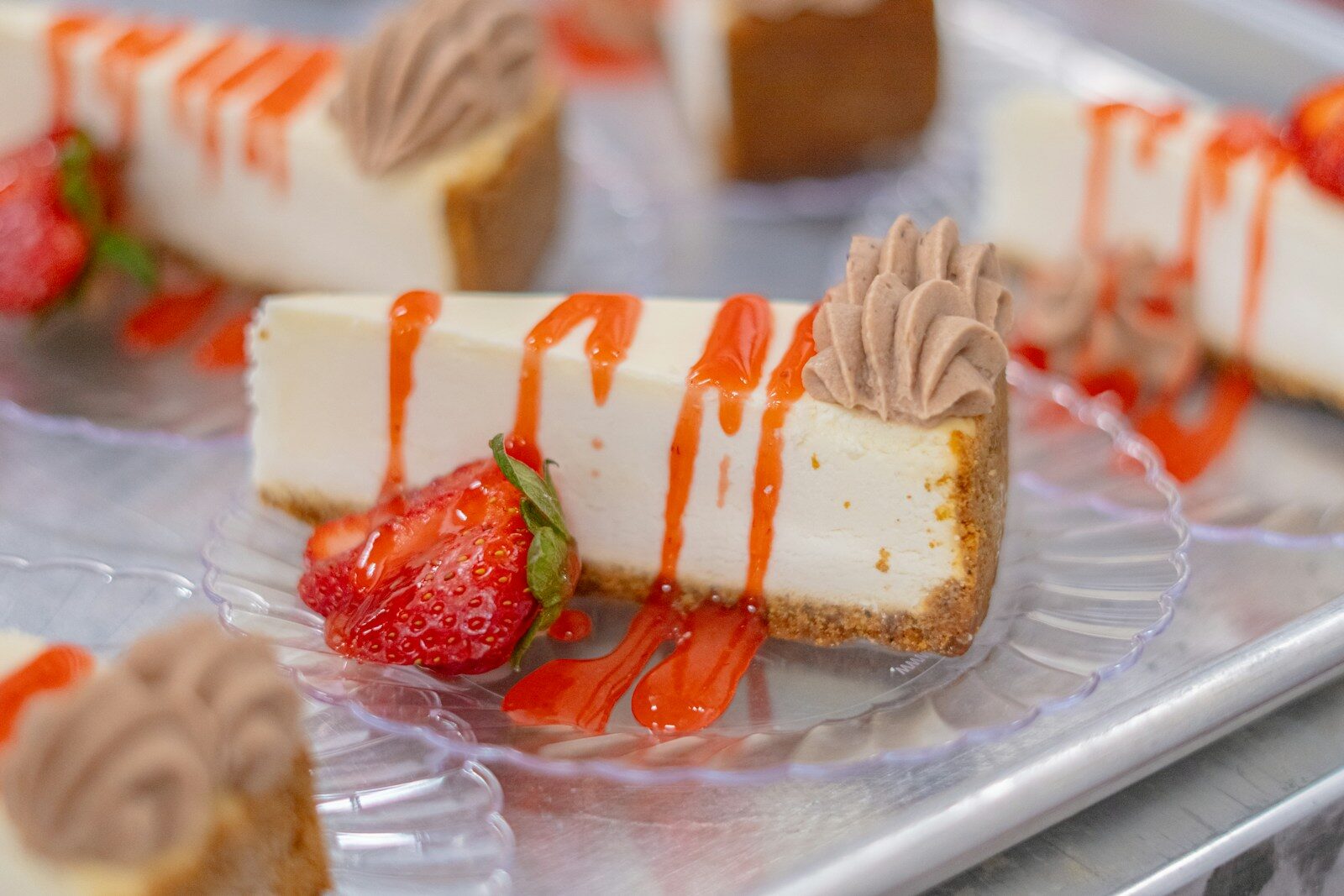 Cheesecake slices are garnished with strawberries and sauce.
