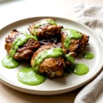 Peruvian grilled chicken thighs drizzled with creamy green sauce on a plate