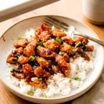 Sesame chicken with glossy sauce, sesame seeds, and scallions served over rice