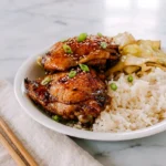 Roasted Asian five-spice chicken thighs with browned skin, served on a plate with scallions.