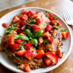 Strawberry basil chicken topped with chopped strawberries and basil on a simple plate