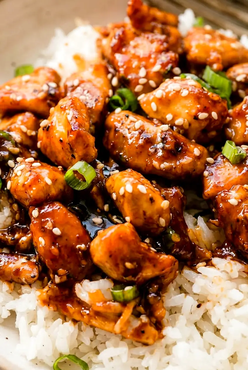 Close-up of sesame chicken pieces coated in glossy sauce with sesame seeds and scallions
