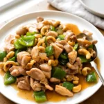 Cashew chicken served on a white plate with glossy sauce and roasted cashews