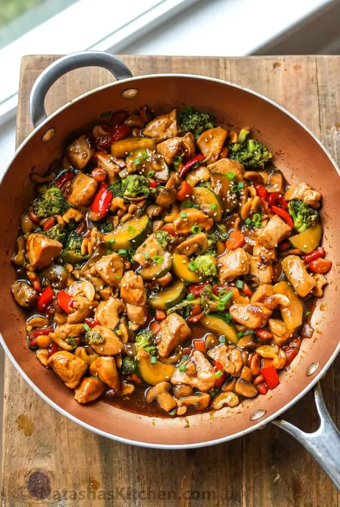 Chicken stir-fry with broccoli, peppers, mushrooms, zucchini, and cashews in a skillet