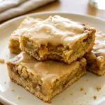 Maple glazed apple blondies cut into squares on a simple plate with glossy glaze