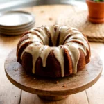 Pumpkin Bundt cake on a wooden cake stand with maple icing and pumpkin pie spice on top