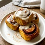 Pumpkin cinnamon rolls topped with maple cream cheese icing on a plate