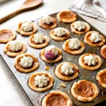Mini pumpkin pies topped with whipped cream in a mini muffin pan