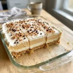 Pumpkin lush squares in a baking dish with whipped topping, toffee bits, and mini chocolate chips