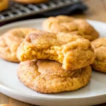 Two stacked pumpkin snickerdoodle cookies, one with a bite missing, on a simple plate