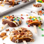 Chocolate covered caramel apple slices topped with candies and nuts on a white marble countertop