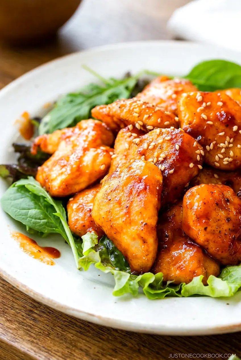 Close-up of honey gochujang chicken showing the glossy sauce and browned chicken pieces over greens