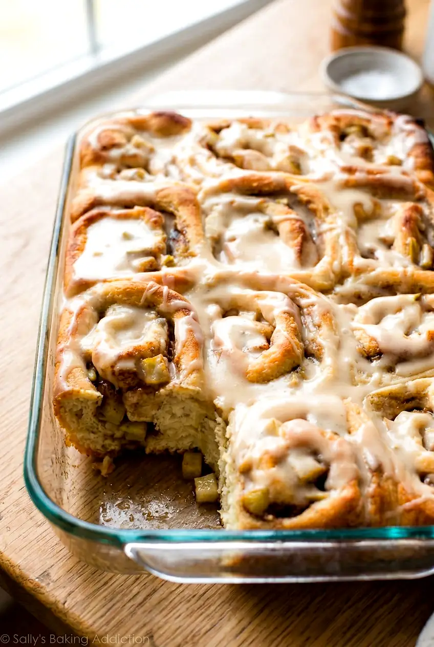 Apple cinnamon rolls in a glass baking dish with one roll slightly separated to show the filling