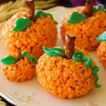 Pumpkin Rice Krispie Treats with pretzel stems and green icing leaves on a cream ceramic platter.