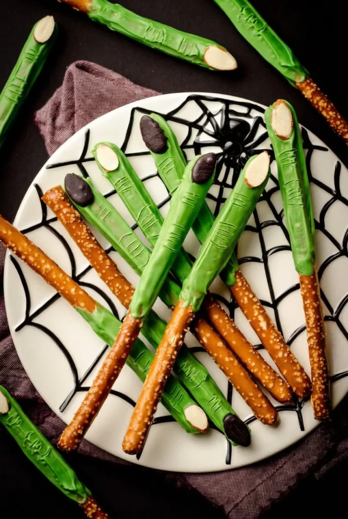 Green witch finger pretzel rods with almond nails on a black spiderweb plate.