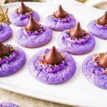 Purple Witch Hat Cookies with chocolate kiss peaks and sprinkle-covered frosting bands on a white platter.
