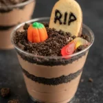 Halloween dirt pudding cup with visible chocolate pudding layers, cookie dirt, RIP tombstone, pumpkin candy, and gummy worm