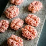 Pale pink Halloween Brain Rice Krispie Treats with red streaks and deep center grooves on a rustic wooden board.