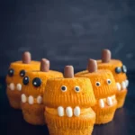 Halloween pumpkin monster cupcakes stacked in pairs with orange frosting mouths, candy eyes, teeth, and brown stems