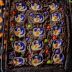 Halloween brookies in a glass baking dish with ghost sugar cookies and colorful candy-coated chocolates.