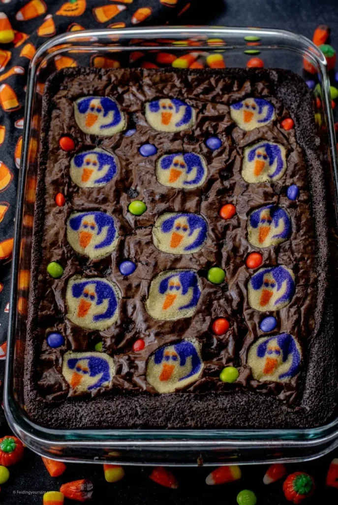 Halloween brookies in a glass baking dish with ghost sugar cookies and colorful candy-coated chocolates.