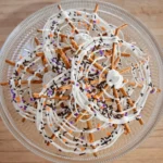 Overlapping Spider Web Pretzels with white candy coating and Halloween sprinkles on a clear glass platter.