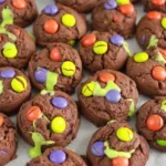Thick chocolate Hocus Pocus Halloween cookies with orange, purple, and green candies and neon-green frosting filling.