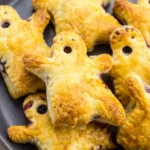 Golden Boo Berry Ghost puff-pastry hand pies piled on a dark platter with blueberry filling visible in face cutouts.