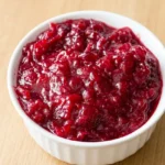 Homemade cranberry sauce with glossy burst berries mounded in a small off-white ceramic bowl.