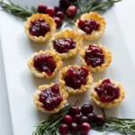 Cranberry Brie mini tarts in crisp fluted phyllo cups on a rectangular platter with rosemary and fresh cranberries.