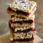 Stacked cranberry crumble bars with golden oat layers, deep red cranberry filling, and powdered sugar