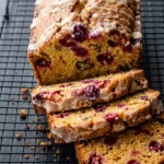 Glazed orange cranberry bread loaf with thick slices showing golden crumb and red cranberry pieces