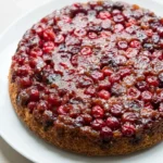 Whole cranberry upside-down cake with glossy ruby berries in dark caramel on a white plate