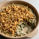 Classic green bean casserole in a shallow beige dish with creamy beans and crisp golden fried onions.
