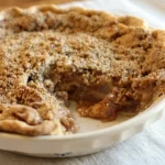 Dutch-style apple crumb pie in a white ceramic dish with a removed wedge showing tender cinnamon apples.
