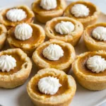 Mini pumpkin pies with golden pastry shells, pumpkin custard, and piped whipped cream on a gray ceramic plate.