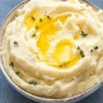 Roasted garlic mashed potatoes in a shallow gray bowl with thyme and melted butter in the center