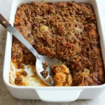 Sweet potato casserole with browned pecan crumble in a white rectangular baking dish with a scooped-out corner.