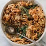 Homemade green bean casserole in an oval cream dish with creamy mushrooms and crisp fried onion strings.