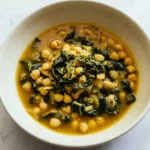 Vegan garlic chickpea soup with kale and nutritional yeast in a pale ceramic bowl