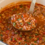 Stuffed pepper soup with beef, rice, red and green peppers, and parsley in a cream Dutch oven.