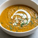 Roasted butternut squash soup in an off-white bowl with cream swirl, toasted pepitas, and parsley.
