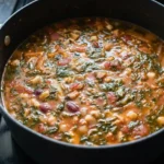 Brothy tomato pasta fagioli with beans, ditalini, diced tomatoes, and spinach in a black Dutch oven.