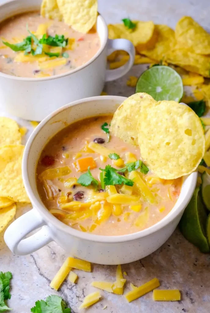 Creamy chicken tortilla soup in a white handled mug with chicken, black beans, corn, cheese, cilantro, and tortilla chips.