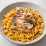 Creamy lemon chicken orzo topped with thick slices of browned parsley-garnished chicken breast.