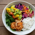 Shrimp avocado mango bowl with white rice, seasoned shrimp, chunky salsa, spinach, cabbage, and crisp vegetables.