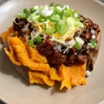 BBQ chicken sweet potato bowl with saucy chicken, melted cheese, and green onions on a cream plate